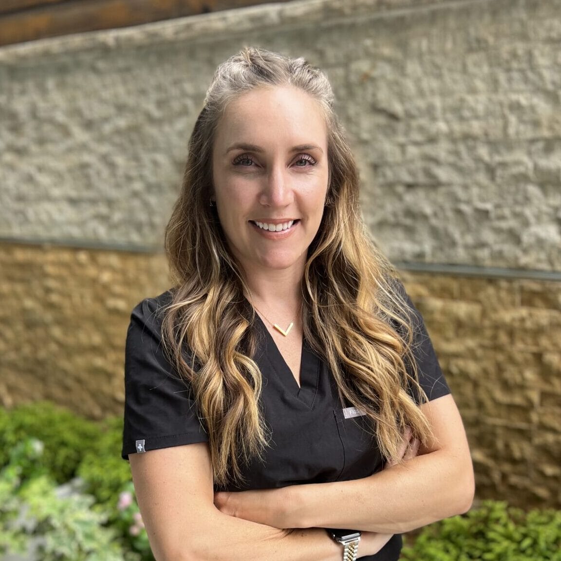 A woman in a black scrub shirt standing in front of a relaxing garden spa.