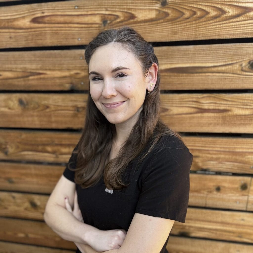 A woman in a black shirt with flawless facial skin standing in front of a wooden wall.