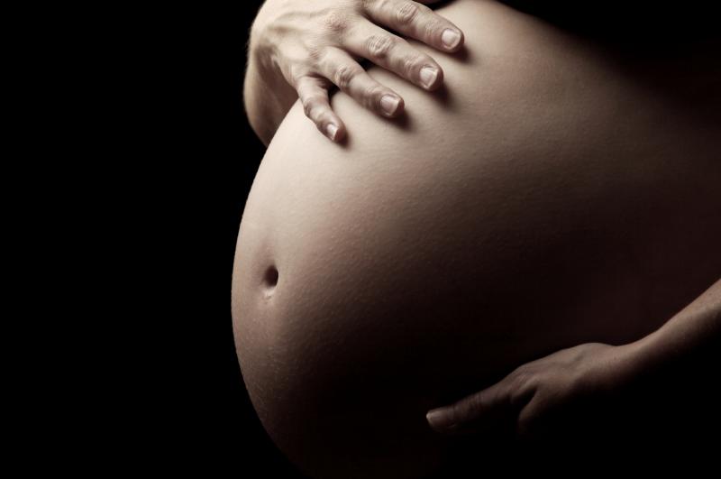 A pregnant woman's belly is shown against a black background, highlighting the skin during this intimate experience.