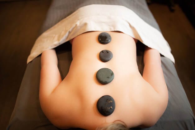 A woman receiving a stone massage for her back, promoting relaxation and skincare.