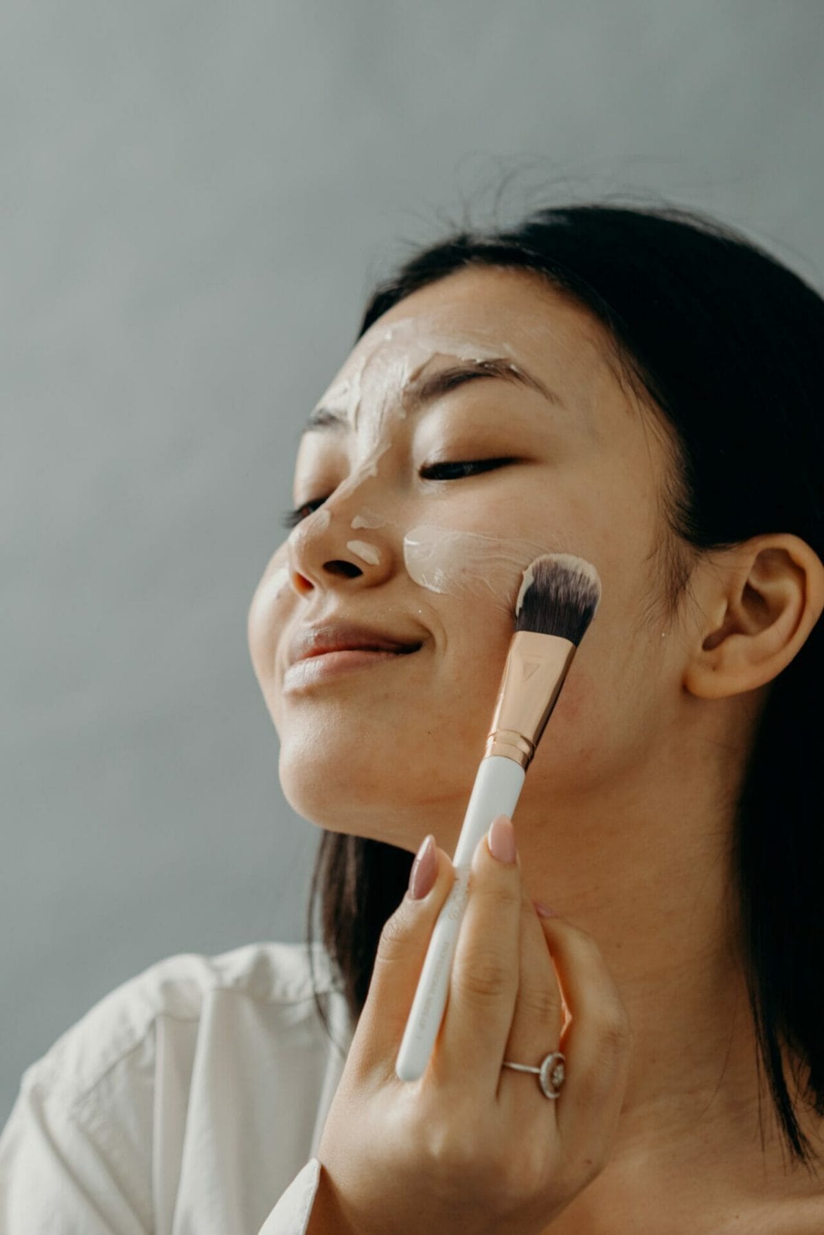 A woman using a brush to properly exfoliate her skin while applying makeup.
