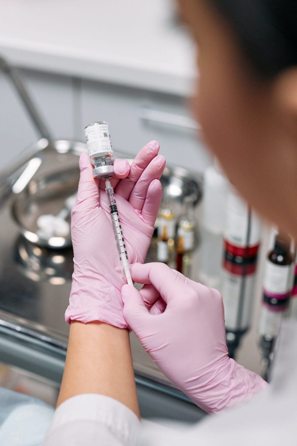 A woman in pink gloves expertly holds a syringe, preparing to administer a cosmetic injectable to a client.