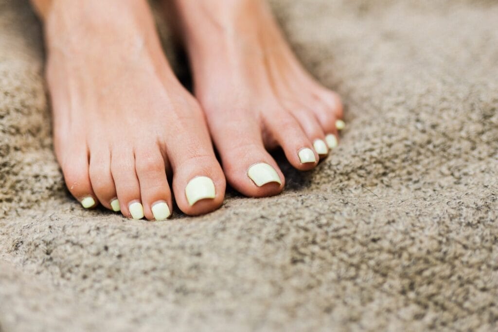 The importance of foot care is evident as a woman's feet, adorned with yellow nails, rest on a soft carpet.