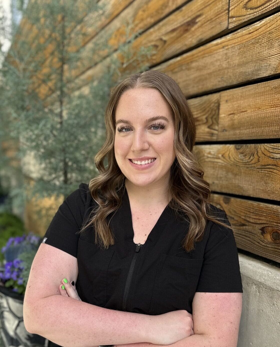 A woman in black scrubs standing in front of a wooden wall, wearing Auto Draft.