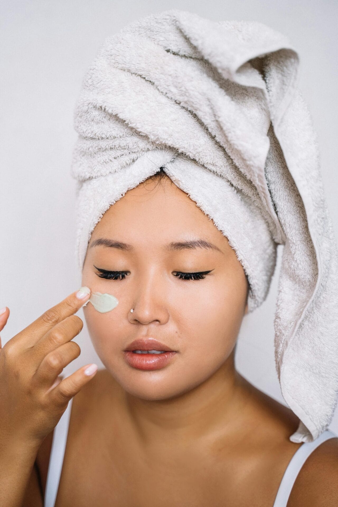 In winter, a woman with a towel on her head is preventing dry skin by applying cream to her face.