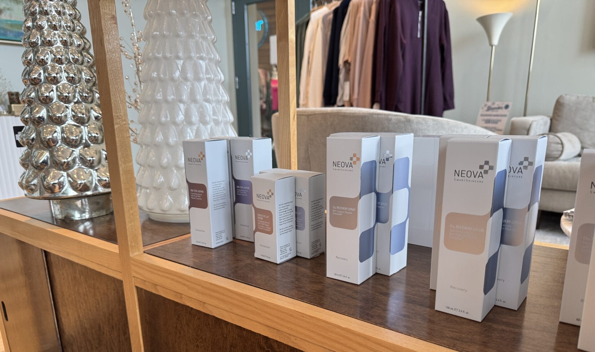 A festive display of Neova skincare products graces a wooden shelf at Center Medspa, surrounded by decorative trees and clothing racks, creating the perfect atmosphere for holiday shopping.