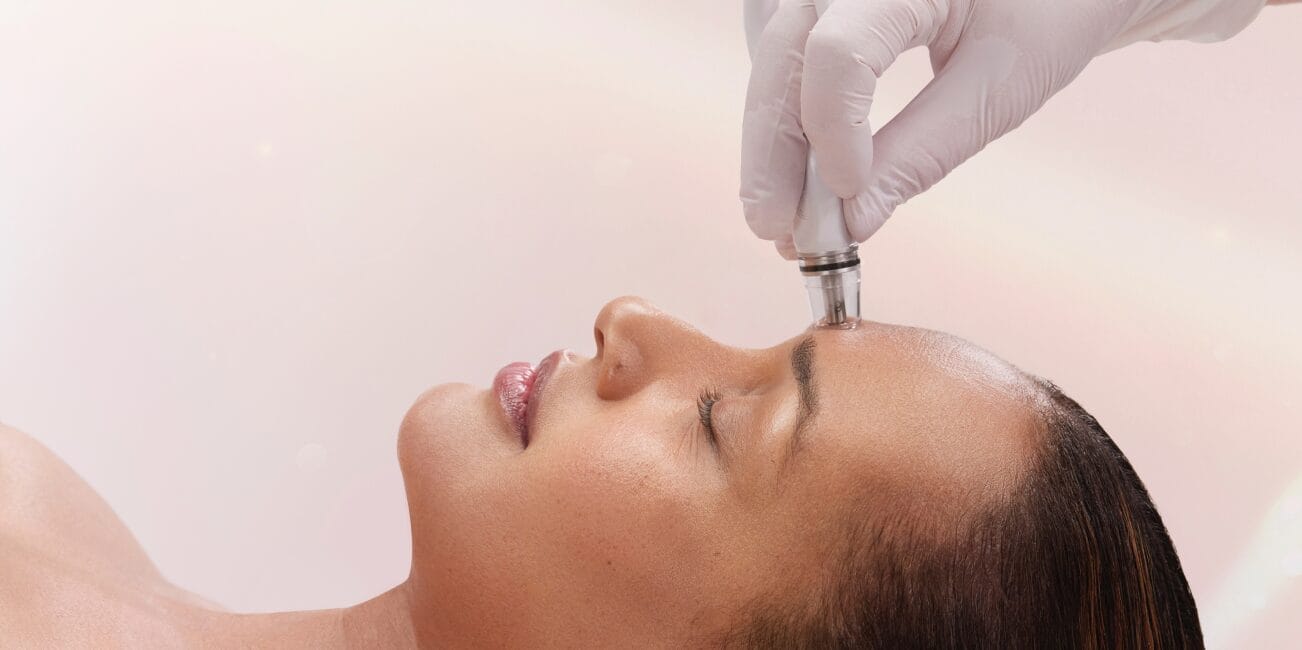 At Center MedSpa, a person indulges in advanced facial treatments as a gloved hand deftly operates a handheld device on their forehead, embracing moments of seasonal relaxation and rejuvenation.