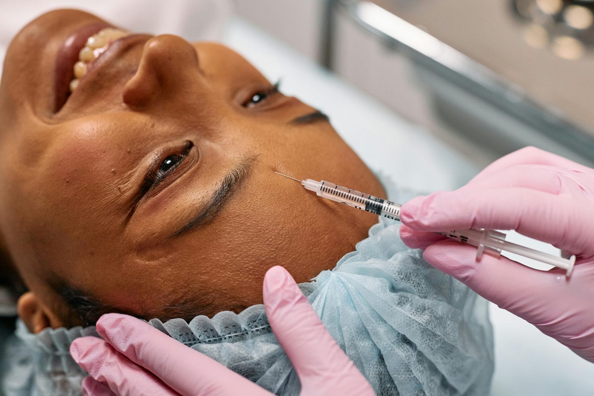 At Center MedSpa, a person lying down receives an injectable treatment in the forehead from a practitioner wearing pink gloves, offering a touch of care that feels as comforting as Christmas.