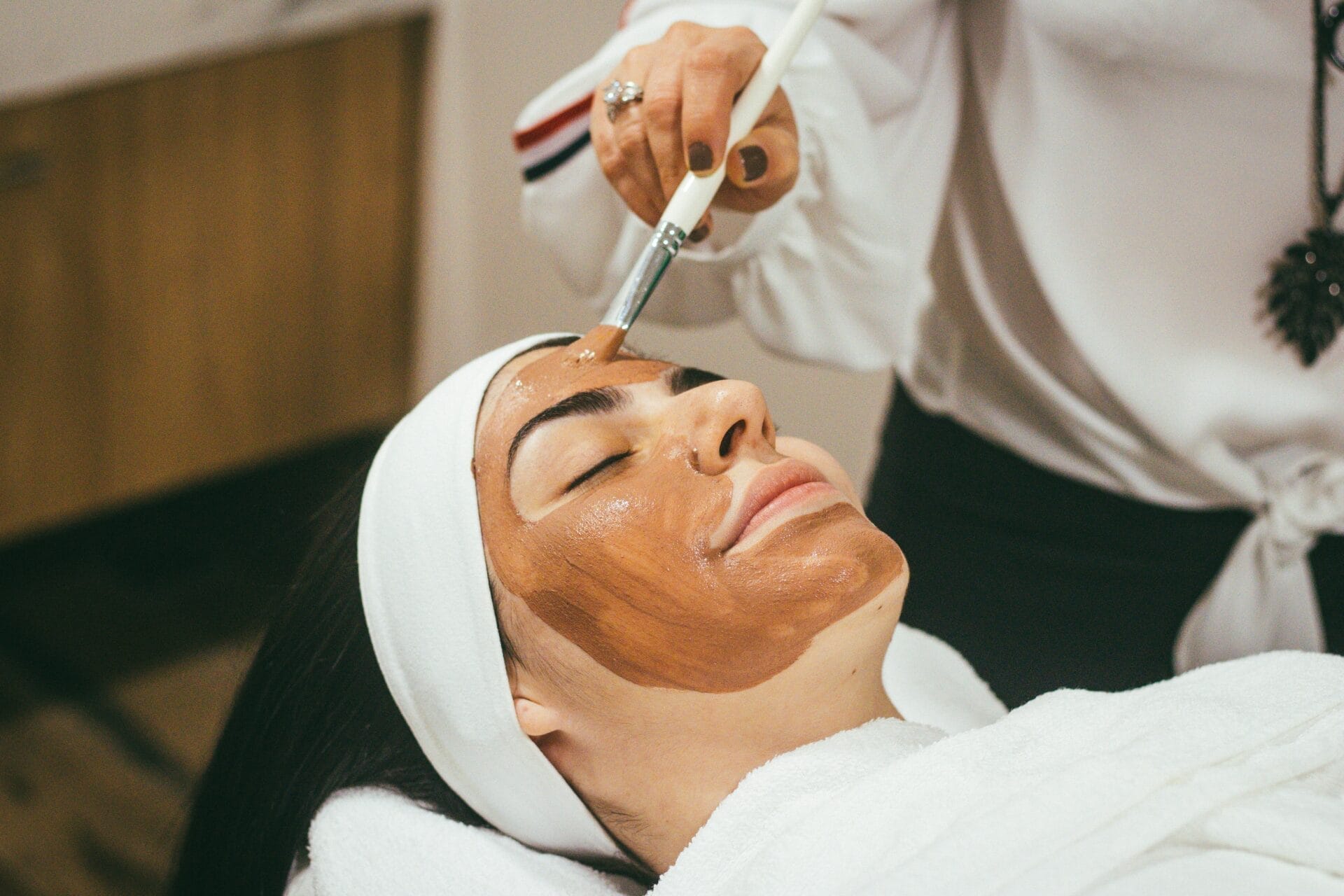 At Center MedSpa, unwind as you lie down with a headband on, enjoying a refreshing facial treatment. A brush gently applies a rich brown mask, offering the ultimate skincare peel. It's like gifting your skin an early Christmas treat!